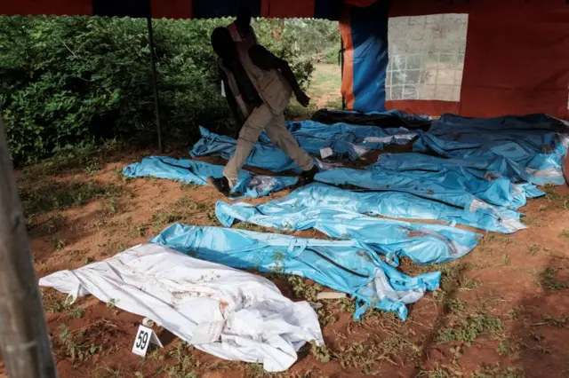 An officer of the Directorate of Criminal Investigations (DCI) walks through exhumed bodies in bodybags on the ground prior to a transport to the mortuary, at the mass-grave site in Shakahola, outside the coastal town of Malindi, on April 25, 2023.