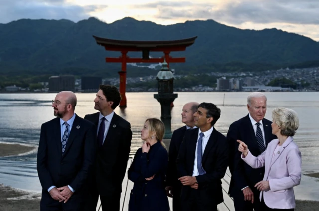 The group posed for photographers against the backdrop of the shrine, water and mountain