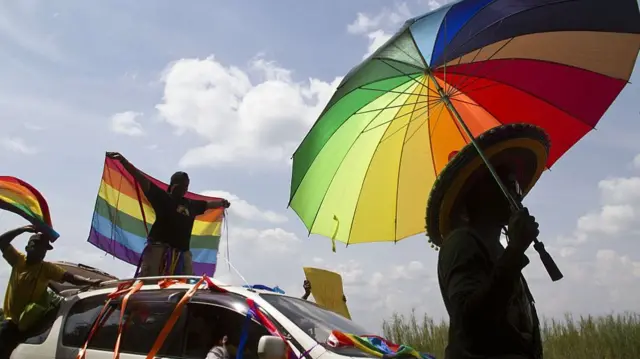 A person holds an umbrella bearing the colours of the rainbow flag as others wave flags during the the first gay pride rally since the overturning of a tough anti-homosexuality law, which authorities have appealed, in Entebbe - August 2014