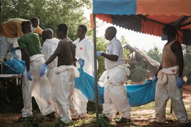 Workers carry the exhumed bodies in bodybags to the mortuary, at the mass-grave site in Shakahola, outside the coastal town of Malindi, on April 25, 2023.