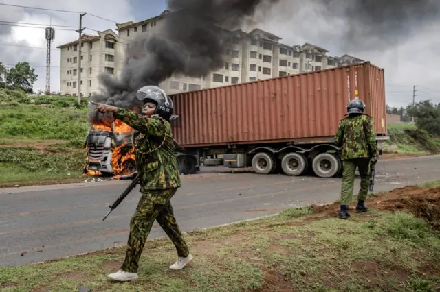 A Kenyan police officer calls for reinforcement in front of a lorry set on fire by protesters during riots in the informal settlement of Kibera in Nairobi - 2 May 2023