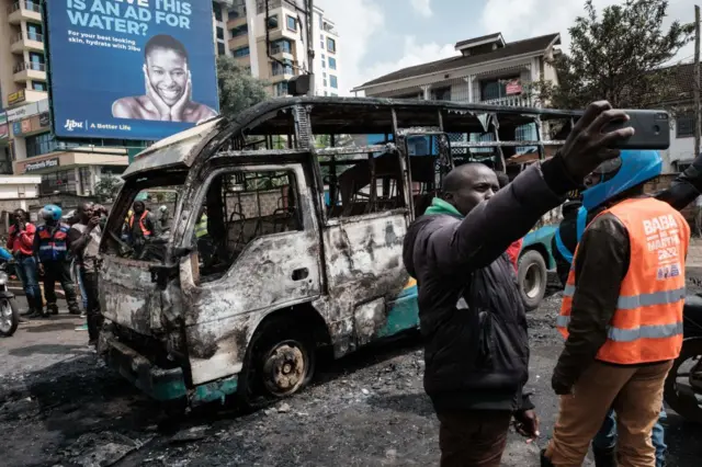 A man takes a selfie in front of a burnt bus as the Kenya opposition leader Raila Odinga's Azimio la Umoja coalition calls for new demonstrations in Nairobi on May 2, 2023.