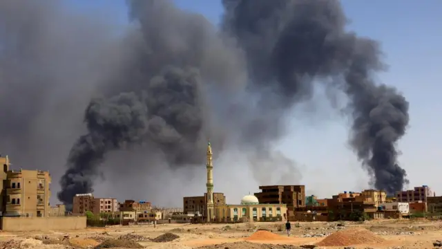 A man walks while smoke rises above buildings after aerial bombardment, during clashes between the paramilitary Rapid Support Forces and the army in Khartoum North, Sudan, 1 May 2023.