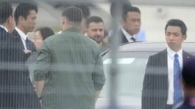 Ukrainian President Volodymyr Zelensky is seen through a fence as he arrives at the Hiroshima airport