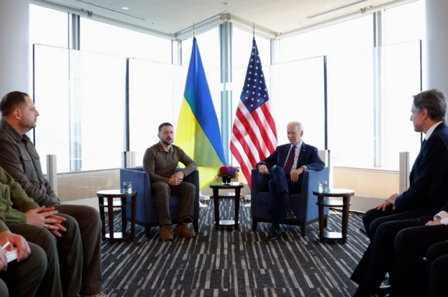 Ukrainian President Volodymyr Zelensky and US President Joe Biden sit at the front of a room facing officials from both nations