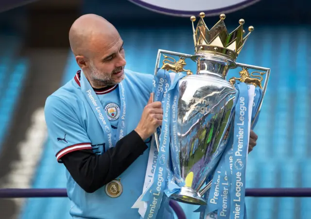 Pep Guardiola looks at the Premier League trophy