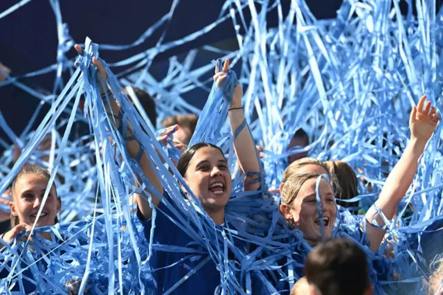 Sam Kerr is covered in blue ticker tape with her arms aloft in celebration.