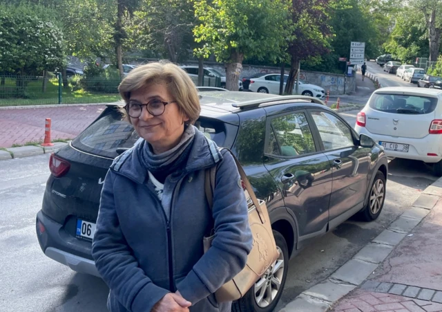 Sengul pictured outside a polling station. She is a middle-aged woman with glasses and a grey coat holding a handbag with parked cars visible behind her