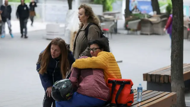 Two women comfort a third, who is sitting on a bench in a Belgrade park