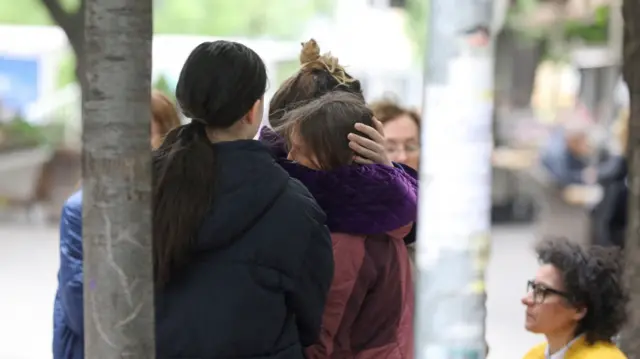 People hugging outside the scene of the shooting