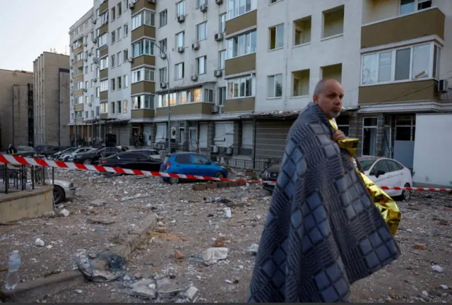 A man stands next to his apartment building in a survival blanket