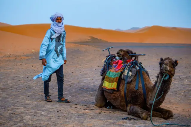 A Berber man stands next to a camel in Sahara Desert