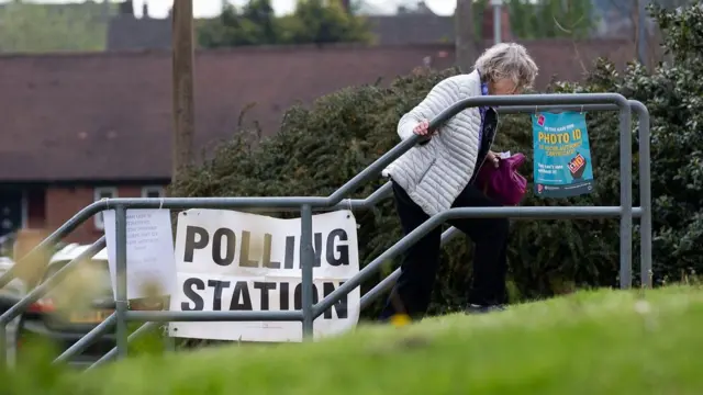 A woman walks up some stairs with a polling station sign in the background