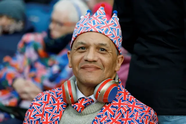 A man in a union jack crown and suit smiles