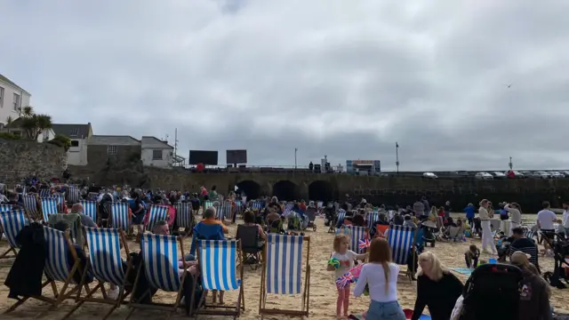 People sit in deckchairs on a beach