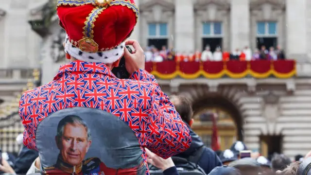 A royal fan takes a photo as Britain's King Charles and Queen Camilla stand on the Buckingham Palace balcon