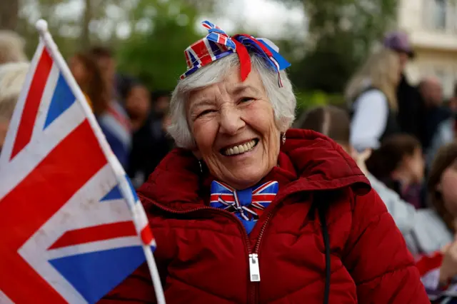 A woman in a union flag hat and bow tie beams