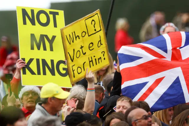 People hold up placards saying "not my king" and "who voted for him?"