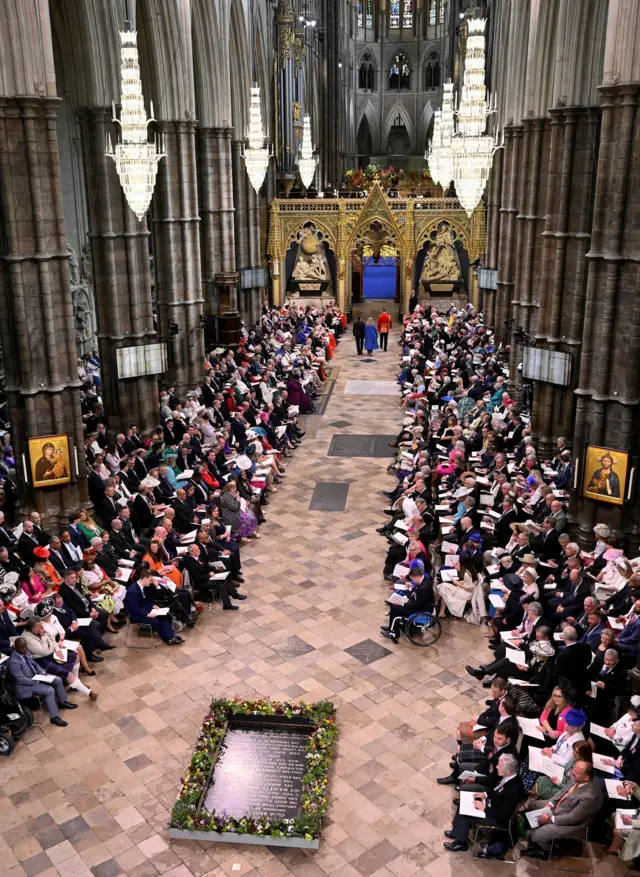 A wide shot of inside Westminster Abbey, with people lining the nave