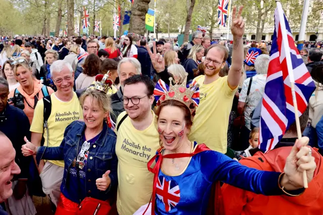 People in "abolish the monarchy" T-shirts pose with smiles next to royal fans