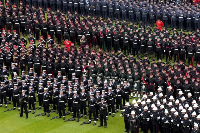 Members of the armed forces stand in formation on the lawn outside Buckingham Palace