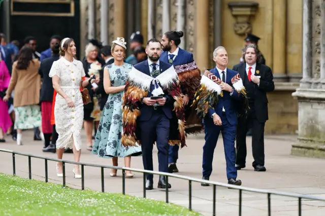 Three men wear feathered capes over their suits as they arrived at the abbey