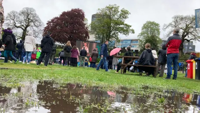 People watch a big screen in Cardiff, with a puddle in the foreground