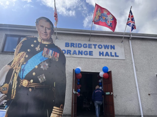 A cardboard cutout of King Charles III in front of a building named Bridgetown Orange Hall