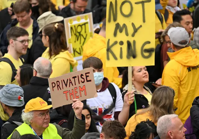 People hold up signs saying "privatise them" and "not my king"