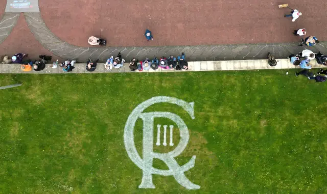 A logo for King Charles is seen on the grass next to people celebrating the Big Lunch on the prom, in Morecambe, Britain, May 7, 2023.