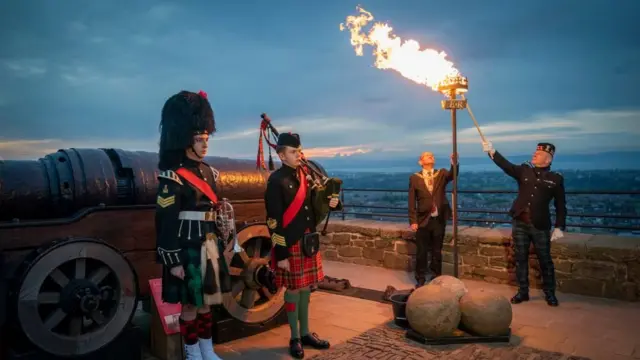 A beacon is lit at Edinburgh Castle with the city in the background