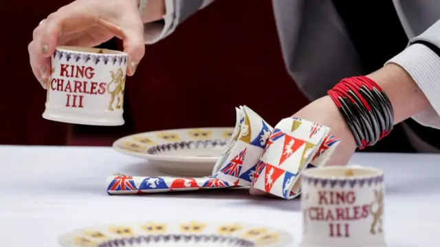 A woman the table with special mugs reading "King Charles III"