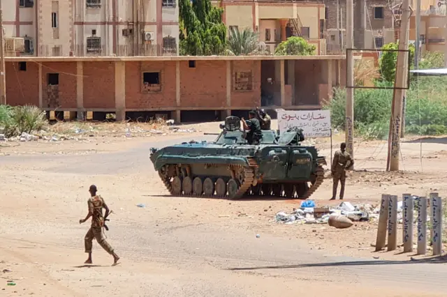 Sudanese Army sodliers walk near armoured vehicles stationed on a street in southern Khartoum, on May 6, 2023, amid ongoing fighting against the paramilitary Rapid Support Forces