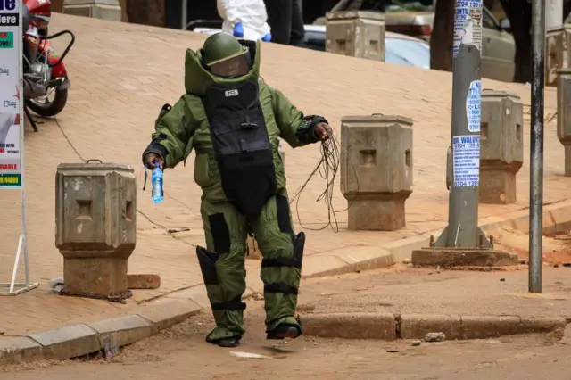 A bomb squad member of the Uganda police prepares to deotnate a suspicious box wrapped with a ribbon, on a fence near the Central Police Station in Kampala, Uganda, on November 16, 2021.