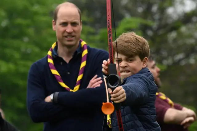 Prince George concentrates hard while aiming his bow - while Prince William looks on