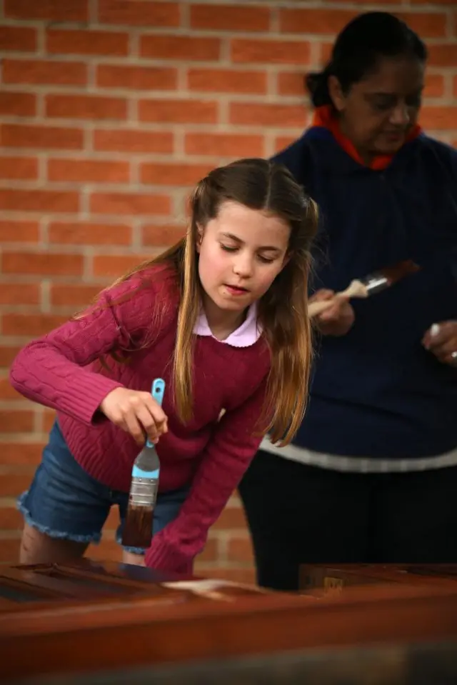 Princess Charlotte uses a brush on some wood