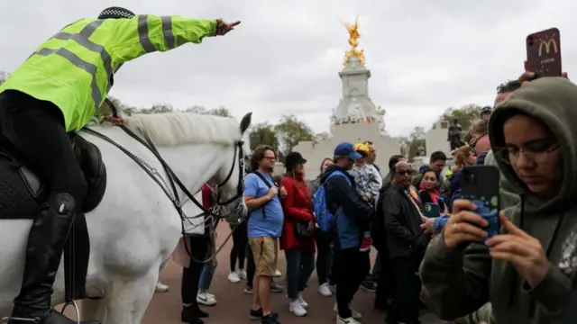 A police officer directs the crowd as tourists jostle to get a glimpse of the changing of the King's Guard