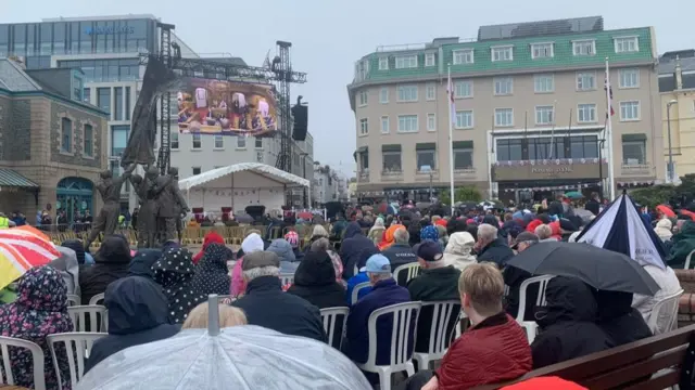 Islanders at Liberation Square watching big screen of states sitting