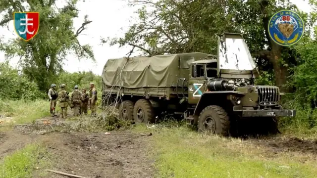 Troops gather near a destroyed vehicle