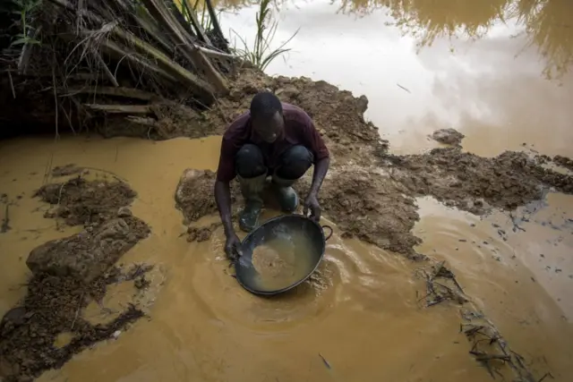 A Galamseyer, an illegal gold panner, washes the soil to check as he looks for speck of gold, in Kibi area, southern Ghana