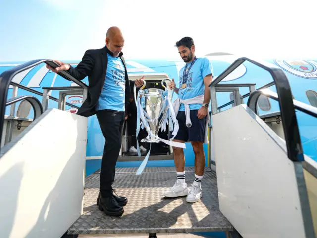 Pep Guardiola and Ilkay Gundogan bring the trophy off the plane