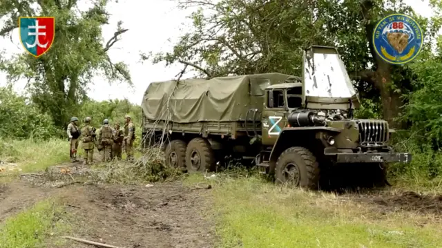 Ukrainian servicemen near a destroyed vehicle in Storozheve