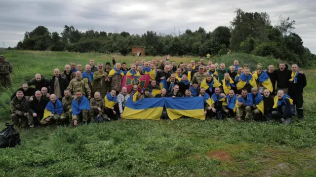 Dozens of Ukrainian prisoners of war pose for a photo with flags