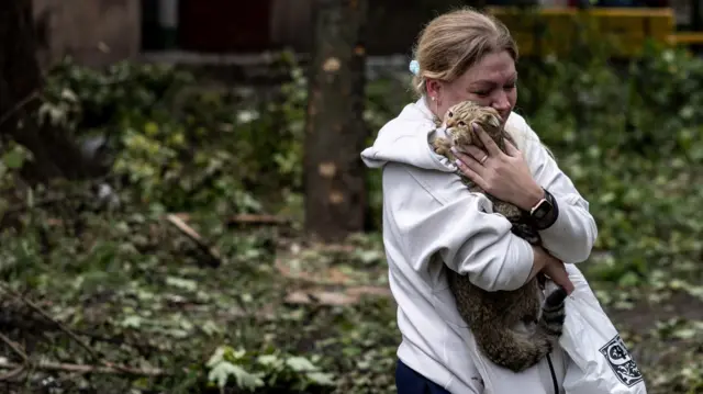 A woman holds her cat at the scene of an apartment block, hit by a Russian missile, in Kryvyi Rih