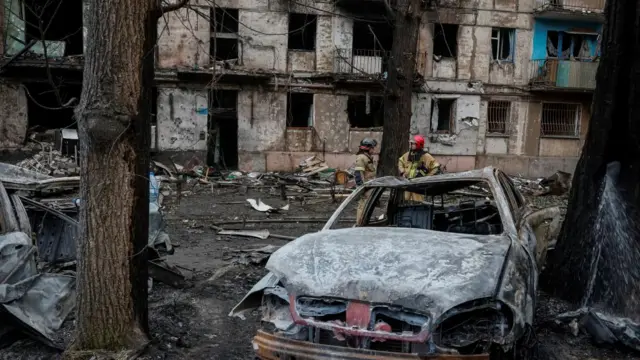 Rescue workers stand near ruined buildings and a burned-out car in Kryvyi Rih