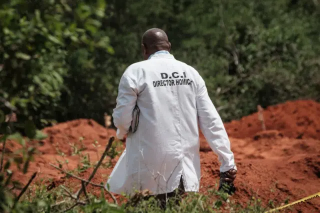 An officer with the Kenyan Directorate of Criminal Investigations (DCI) walks next to dug up ground at the mass-grave site in Shakahola, outside the coastal town of Malindi, on April 25, 2023.