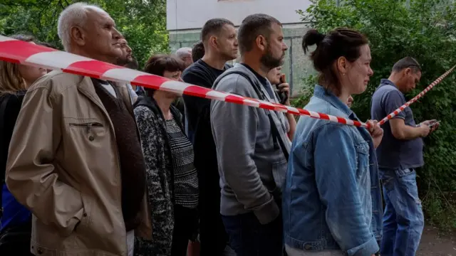 People stand behind a cordon in Kryvyi Rih after a Russian missile strike