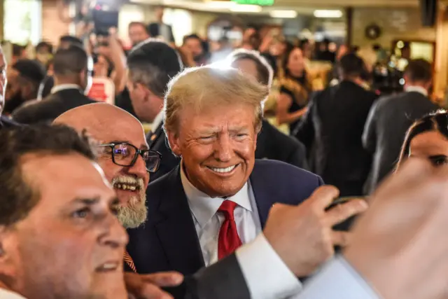 Trump poses for photos with supporters in a restaurant.