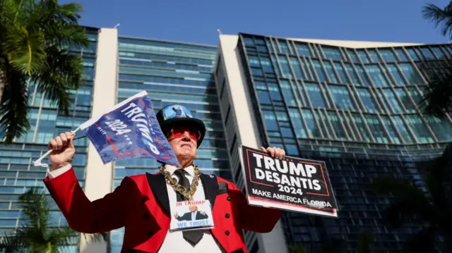 A Trump supporter holds a flag and placard emblazoned with the words "Trump 2024"