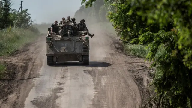 Ukrainian troops ride atop an armoured vehicle